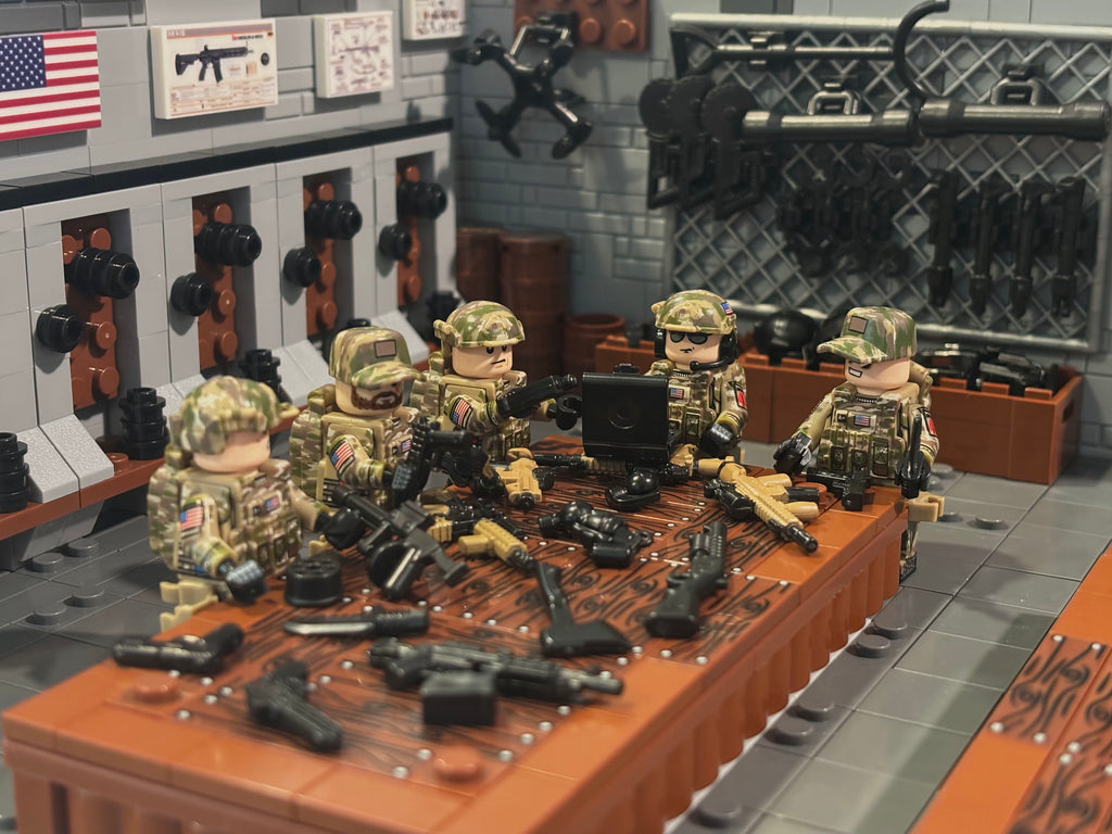 A detailed LEGO-style diorama of a tactical weapons station, featuring minifigures in camouflage uniforms seated around a table covered with various toy firearms and accessories, with a weapon rack and American flag in the background. Fabled Figs