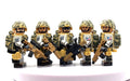 Five toy soldier minifigures in tan and green camouflage uniforms holding rifles, arranged side by side on a white surface against a white background. Fabled Figs