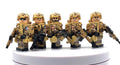 Five toy soldier minifigures in desert camouflage uniforms and helmets, each holding a black rifle, displayed on a white circular pedestal against a white background. Fabled Figs